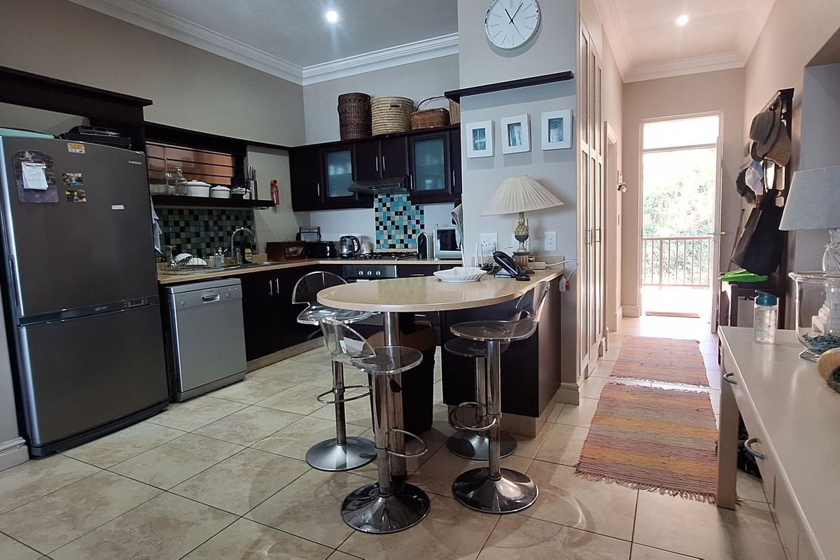 A functional kitchen featuring dark cabinetry, a tiled backsplash, and a built-in breakfast bar, with direct access to an outdoor balcony area.