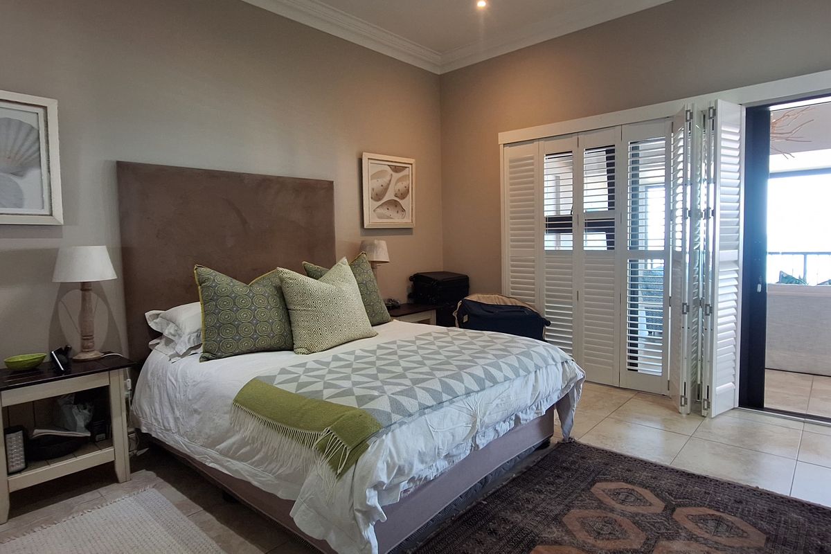 Spacious bedroom featuring tiled flooring, crown molding, and bi-fold plantation shutters providing direct access to an outdoor balcony area.