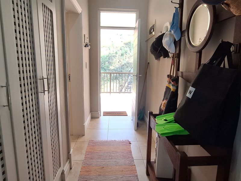 A bright hallway featuring built-in storage cupboards and tiled flooring, leading directly to an exterior balcony entrance.