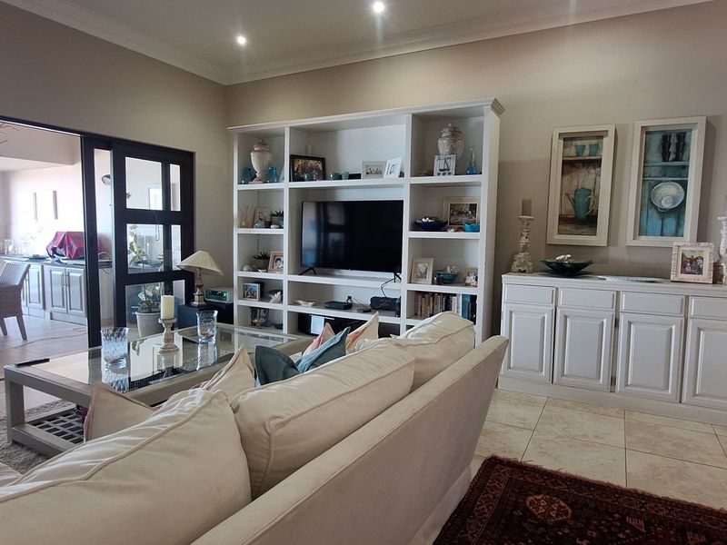 Spacious living room featuring tiled flooring, recessed lighting, crown molding, and a large built-in shelving unit, with seamless access to an outdoor patio area.