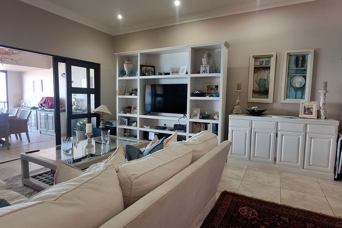 Spacious living room featuring tiled flooring, recessed lighting, crown molding, and a large built-in shelving unit, with seamless access to an outdoor patio area.