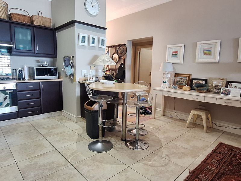Open-plan kitchen and living area featuring dark cabinetry, mosaic backsplash, built-in appliances, and neutral tiled flooring throughout the space.