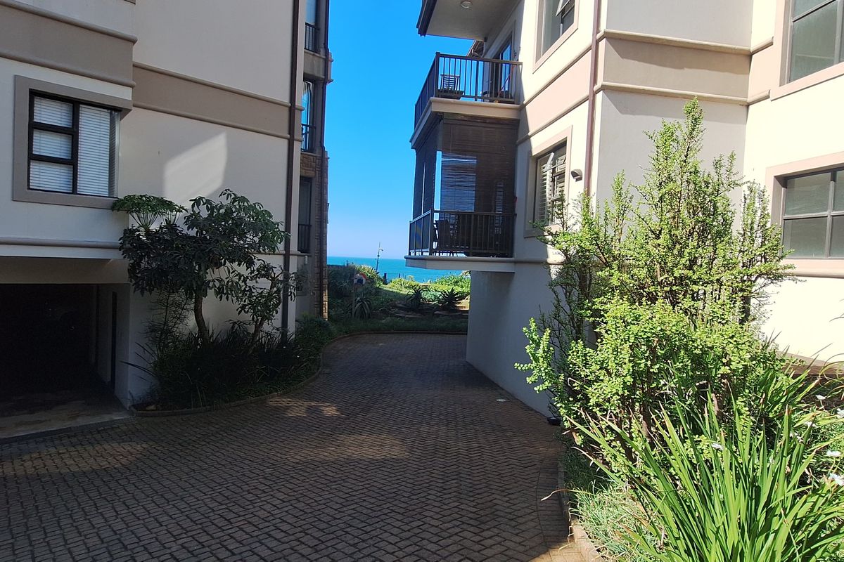 View of the apartment complex exterior featuring a paved driveway between buildings and a balcony overlooking the coastal area.