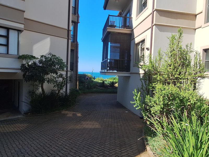 View of the apartment complex exterior featuring a paved driveway between buildings and a balcony overlooking the coastal area.