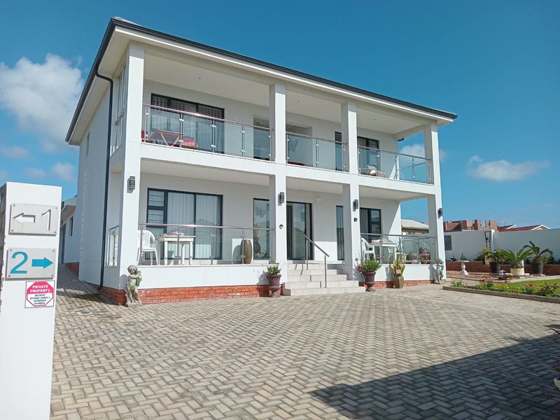 A modern double-story residential property featuring a paved driveway, covered balconies with glass balustrades, and large sliding door access points.