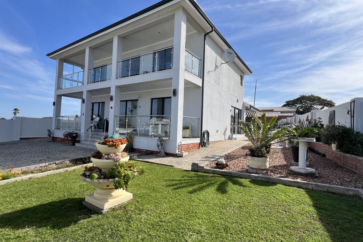Rear view of a modern double-story house featuring glass balustrades, a paved patio area, and a well-maintained garden.