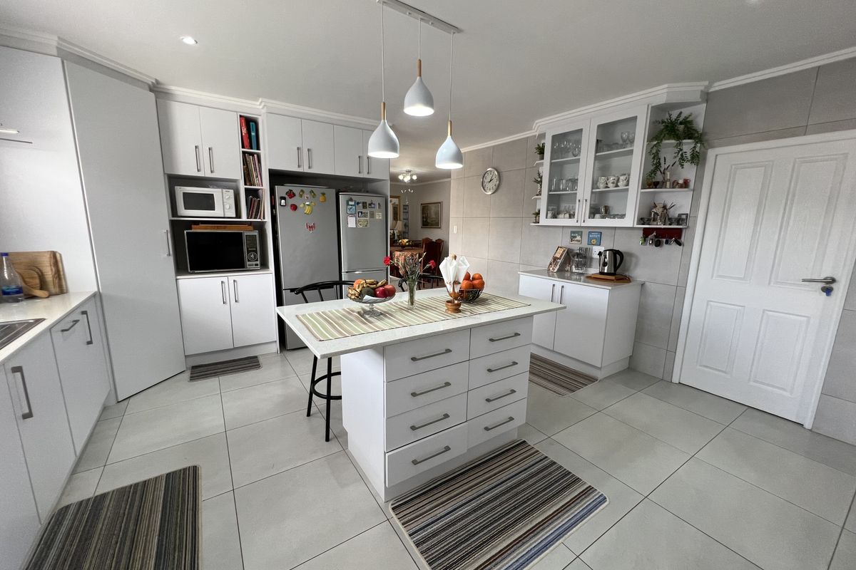 Modern kitchen featuring a central island, white cabinetry, glass-front display units, and tiled flooring with integrated pendant lighting.