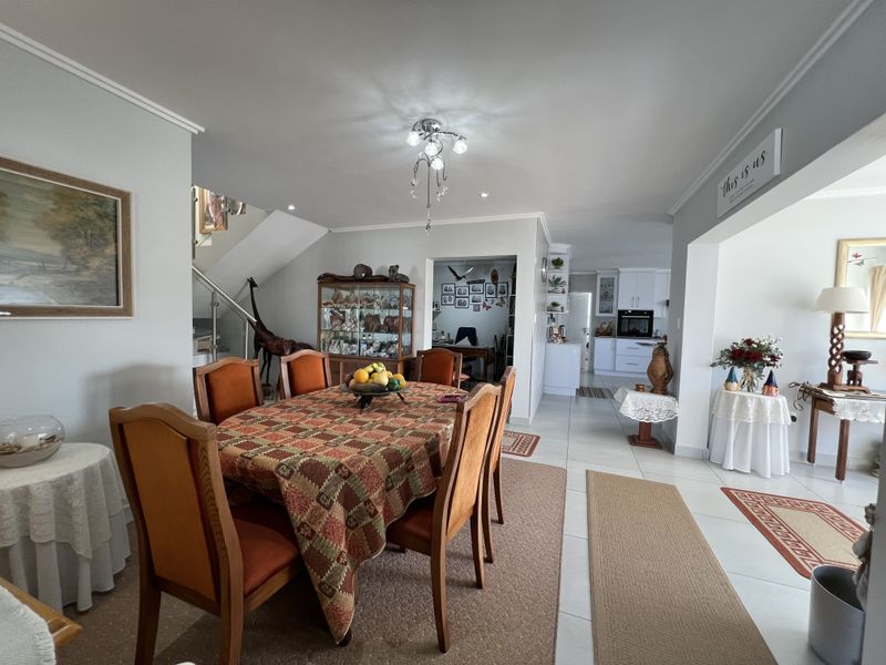 Spacious open-plan dining area featuring tiled floors, a modern staircase with glass balustrade, and a view through to the kitchen.