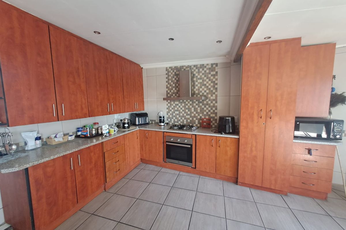 A functional kitchen featuring wood-finish cabinetry, granite countertops, a gas hob with extractor fan, and tiled flooring.