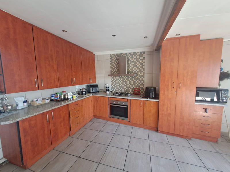 A functional kitchen featuring wood-finish cabinetry, granite countertops, a gas hob with extractor fan, and tiled flooring.