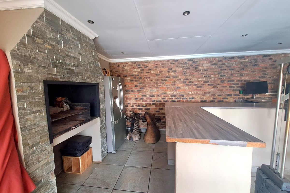 Living area featuring a built-in braai with stone cladding, exposed brick feature wall, and a breakfast bar with laminate countertop.