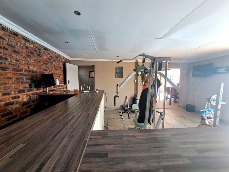 A multi-purpose room featuring a built-in bar counter, exposed brick wall, and tiled flooring, currently utilized as a home gym space.