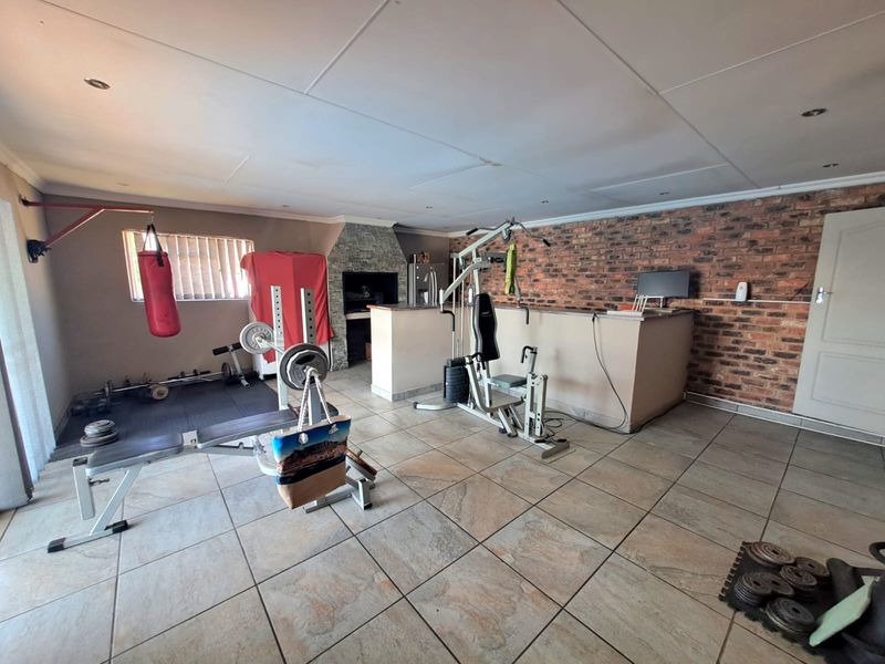 Spacious gym area featuring tiled flooring, an exposed brick feature wall, and a built-in indoor braai facility.