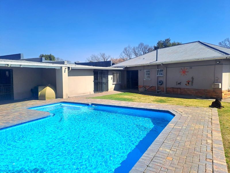 Outdoor pool area featuring a paved deck, swimming pool, and access to the rear of the property with security bars on windows.