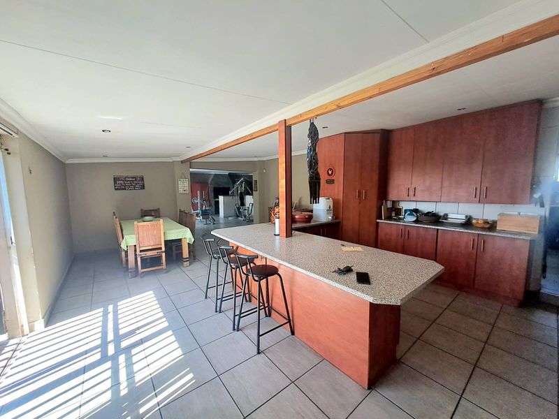 Open plan kitchen and dining area featuring wooden cabinetry, a central island with stone countertop, and tiled flooring throughout.