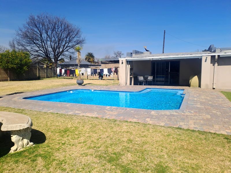 Outdoor pool area featuring a paved surround, a covered patio space, and a concrete garden bench set within a lawned backyard.