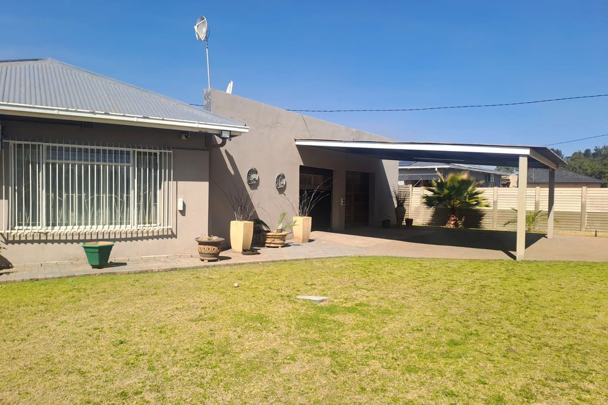 Rear view of the property featuring a lawn, paved area, carport, and secure window bars.