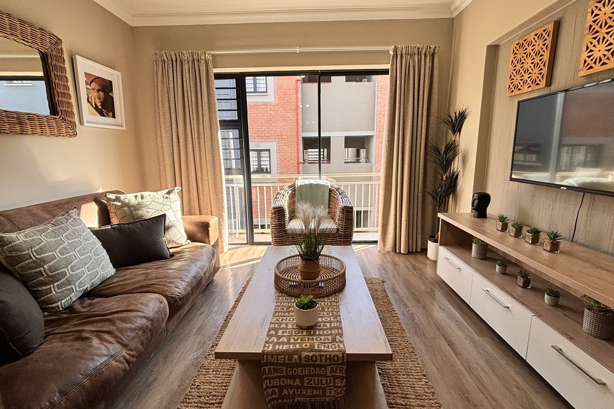 A well-maintained living room featuring laminate flooring, a built-in media console, and a sliding glass door providing access to the balcony.