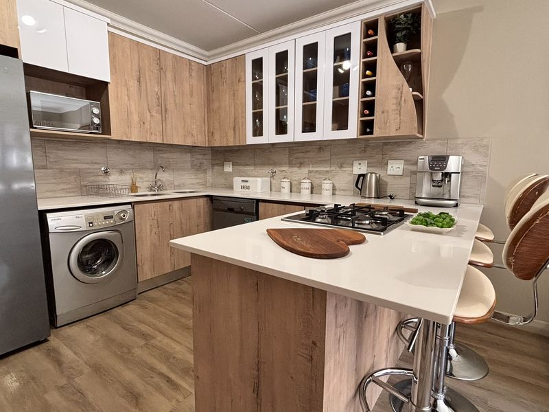 Modern kitchen featuring wood-finish cabinetry, stone countertops, a gas hob, and integrated appliances, offering a functional and stylish cooking space.