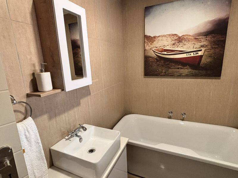A compact bathroom featuring a modern vessel sink, a bathtub, and neutral wall tiling, creating a clean and functional space.