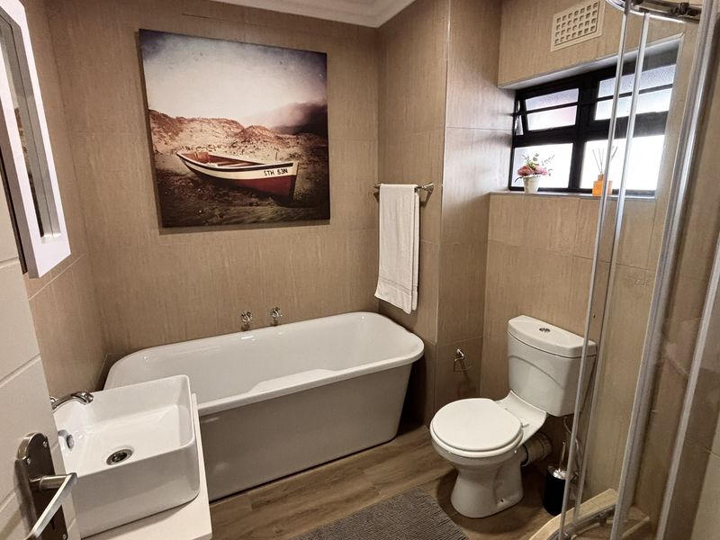 Modern bathroom featuring a freestanding bathtub, vessel sink, separate shower enclosure, and neutral wall tiling, creating a clean and functional space.
