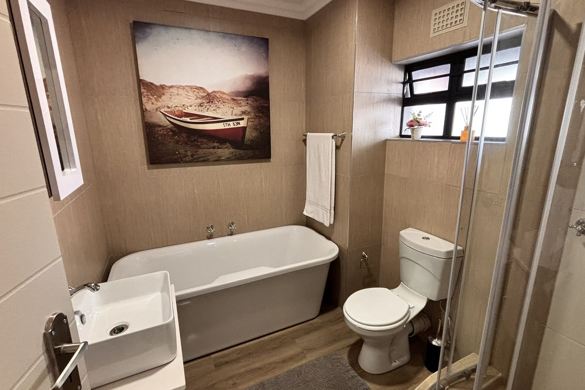 Modern bathroom featuring a freestanding bathtub, vessel sink, separate shower enclosure, and neutral wall tiling, creating a clean and functional space.