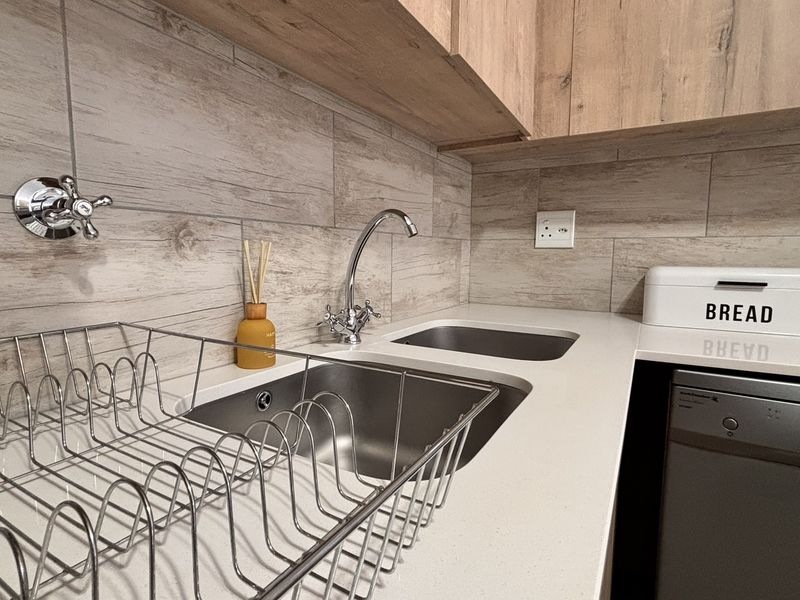 Modern kitchen area featuring wood-look cabinetry, stone countertops, a stainless steel sink, and a tiled backsplash.