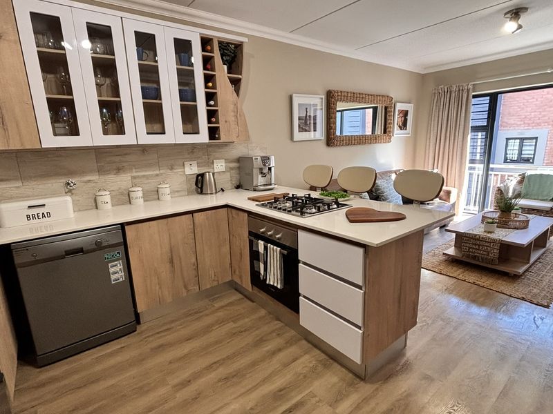 Modern open-plan kitchen and living area featuring wood-finish cabinetry, stone countertops, gas hob, and direct access to a private balcony.