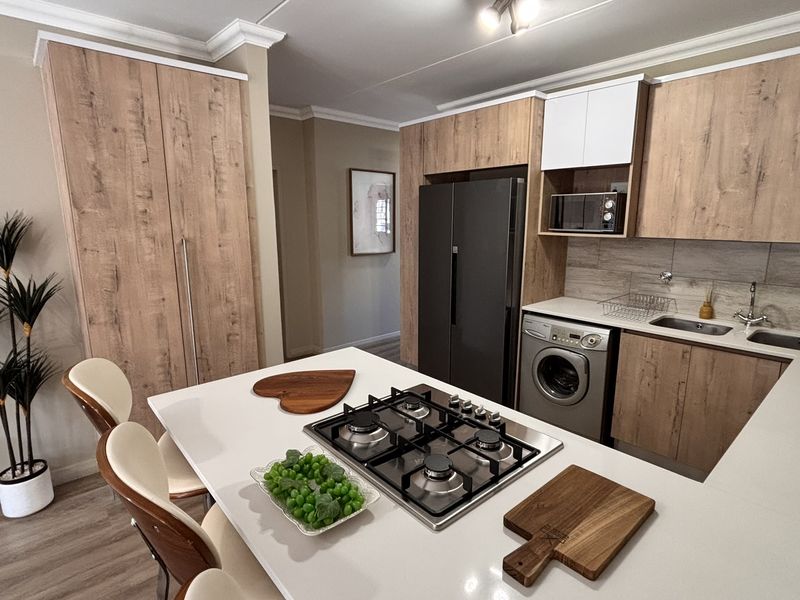 Modern kitchen featuring wood-grain cabinetry, stone countertops, a central island with a gas hob, and integrated appliances including a washing machine.