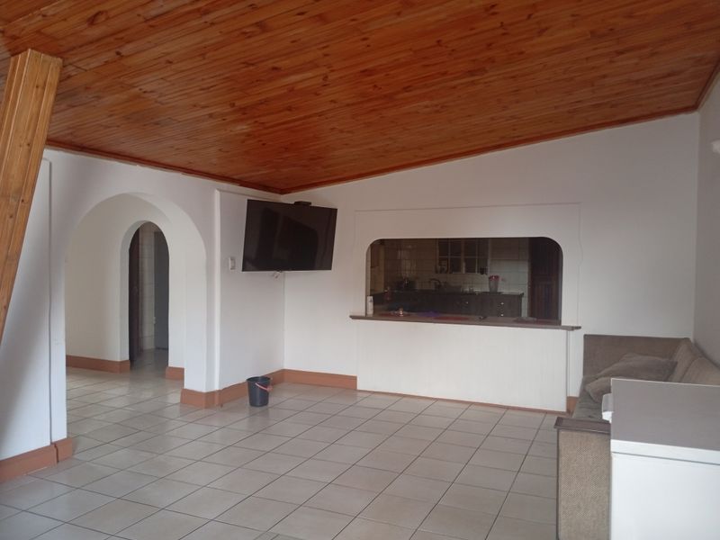 Open plan living area featuring a timber ceiling, tiled flooring, and a convenient serving hatch connecting to the kitchen space.