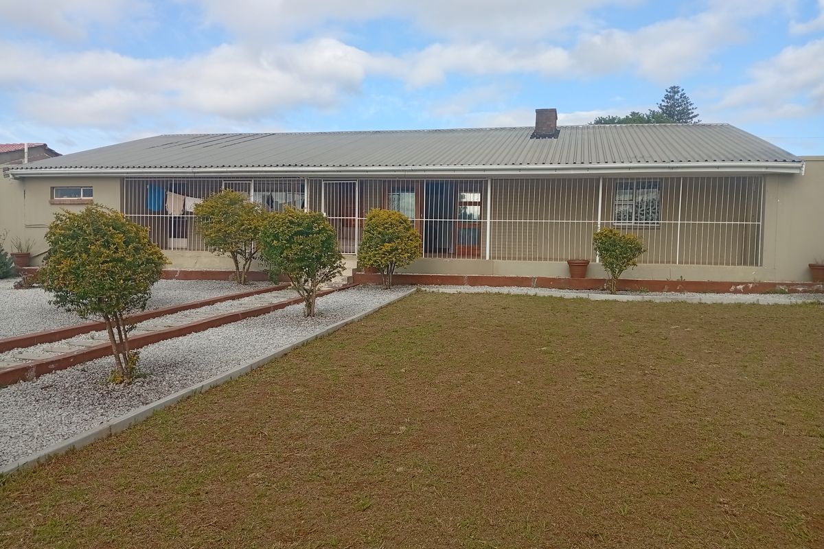 Rear view of a single-story house featuring a corrugated metal roof, brick chimney, and security-barred windows overlooking a gravel and lawn garden.