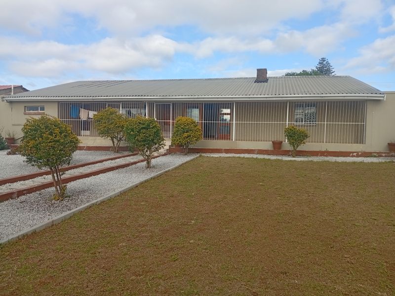 Rear view of a single-story house featuring a corrugated metal roof, brick chimney, and security-barred windows overlooking a gravel and lawn garden.