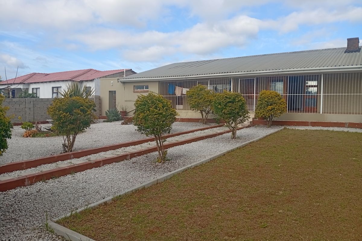 Rear view of the property featuring a corrugated metal roof, security bars on windows, and a low-maintenance gravel and lawn garden area.