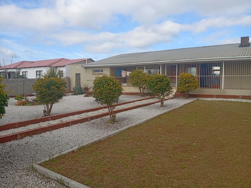 Rear view of the property featuring a corrugated metal roof, security bars on windows, and a low-maintenance gravel and lawn garden area.
