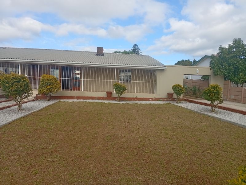 Rear view of the property featuring a corrugated metal roof, security bars on windows, and a private garden area with a lawn.