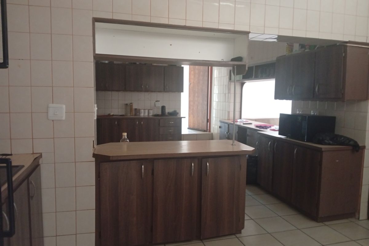 A dated kitchen featuring dark wood-look cabinetry, tiled walls, and a breakfast bar counter, offering potential for a modern renovation.