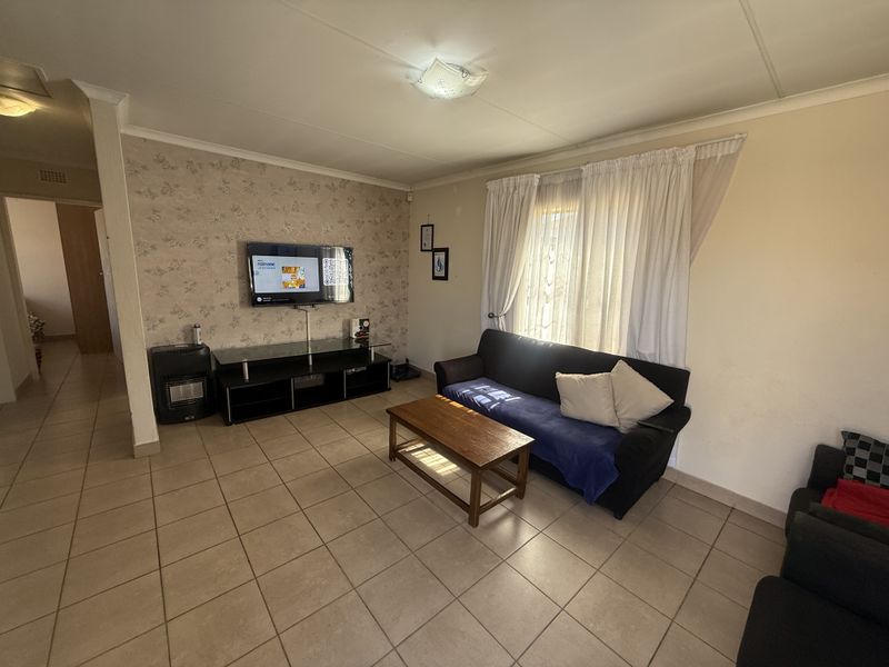 A living room featuring tiled flooring, a built-in gas heater, and patterned wallpaper, offering a functional space with potential for cosmetic updates.