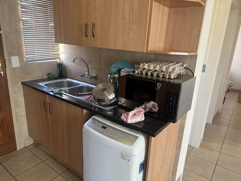 A functional scullery area featuring laminate cabinetry, granite countertops, a double bowl sink, and tiled finishes, providing practical utility space.