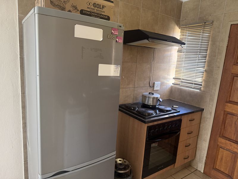 A compact kitchen area featuring built-in cabinetry, an electric hob with extractor fan, and tiled wall finishes.