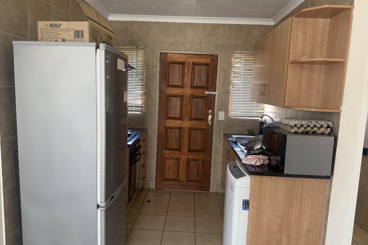 A functional kitchen featuring tiled walls and flooring, built-in wooden cabinetry, granite countertops, and a solid wooden exterior door.