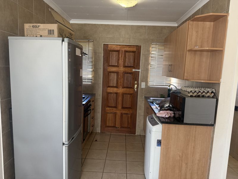 A functional kitchen featuring tiled walls and flooring, built-in wooden cabinetry, granite countertops, and a solid wooden exterior door.