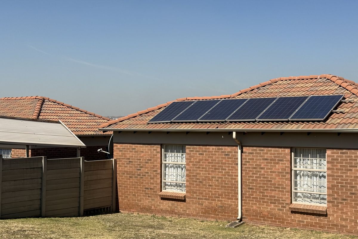 Rear view of a brick house featuring a tiled roof equipped with solar panels, security bars on windows, and a precast concrete boundary wall.