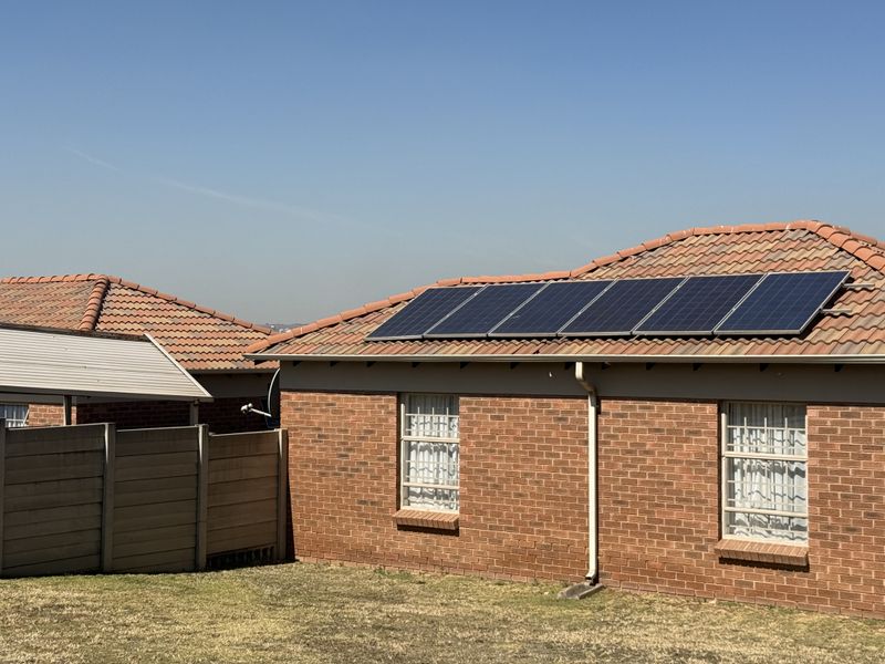 Rear view of a brick house featuring a tiled roof equipped with solar panels, security bars on windows, and a precast concrete boundary wall.