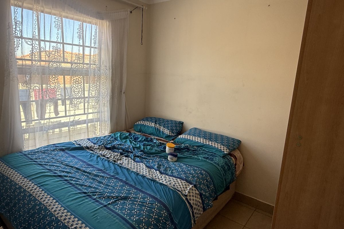 A functional bedroom featuring tiled flooring, a built-in wardrobe, and a window with security bars, offering a practical living space.