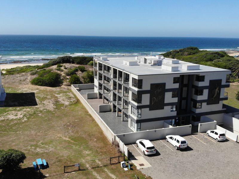 Aerial view of a multi-story apartment complex situated near the coastline, featuring a paved parking area and direct ocean views.
