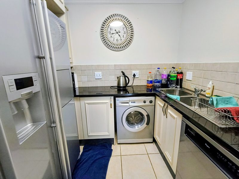 Compact kitchen featuring granite countertops, tiled backsplash, built-in cabinetry, and integrated space for laundry appliances.