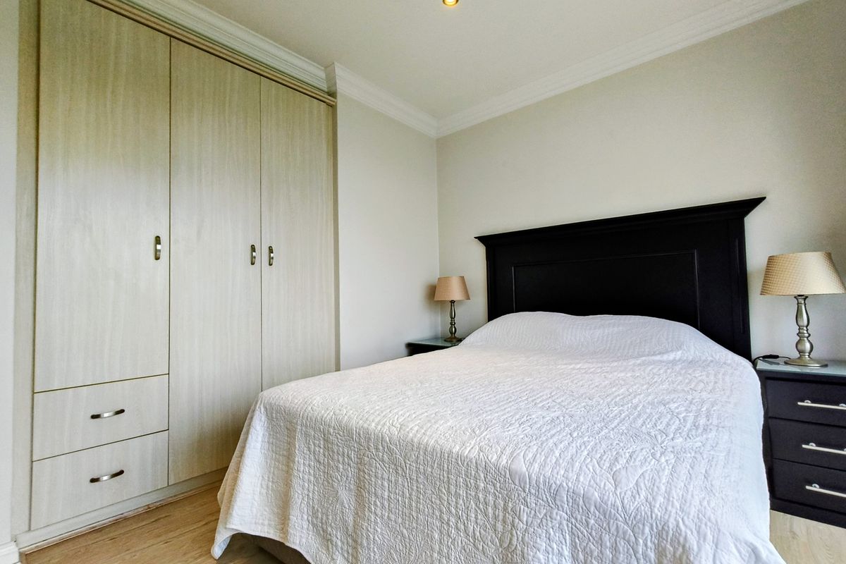 A well-maintained bedroom featuring light wood-finish built-in cupboards, recessed ceiling lighting, decorative coving, and laminate flooring.