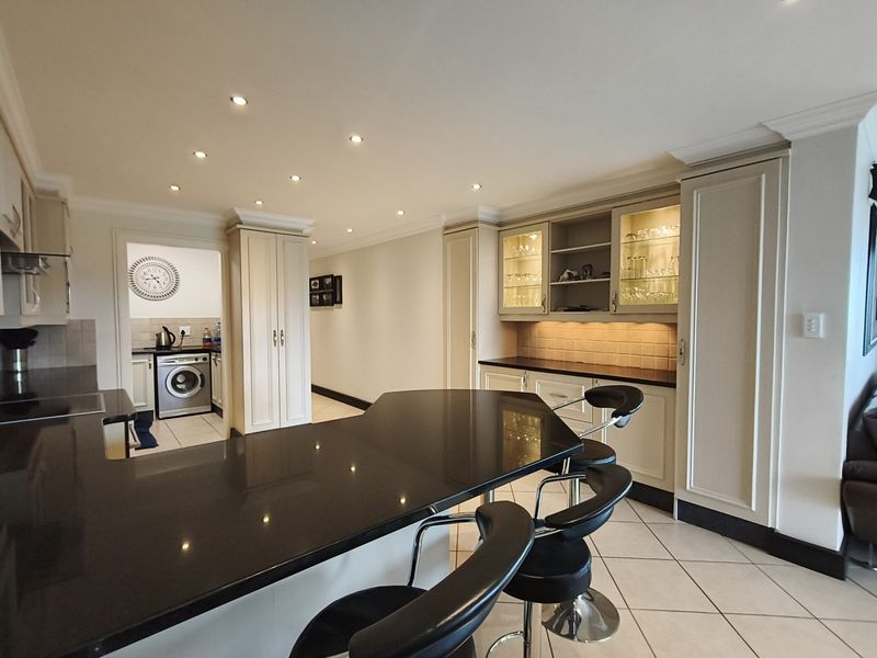 Modern kitchen featuring dark granite countertops, ample built-in cabinetry, glass-front display units, and a breakfast bar, with a separate laundry area visible.