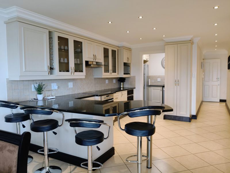 Modern kitchen featuring granite countertops, built-in appliances, ample cabinetry, and tiled flooring, with an open-plan layout and recessed lighting.