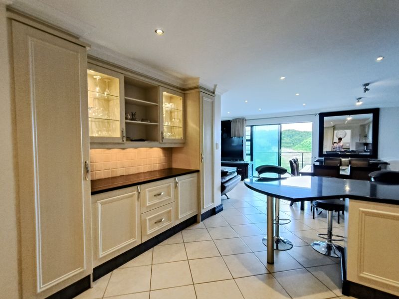 Spacious open-plan living area featuring a well-appointed kitchen with built-in cabinetry, stone countertops, and seamless flow to the outdoor balcony area.